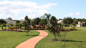 A curved pathway in a well-maintained grassy area with small trees and flower beds. - Indian Creek 2612 (Kissimmee)