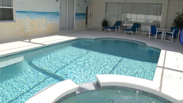 An indoor swimming pool with clear water, surrounded by lounge chairs and a mural of a beach scene.