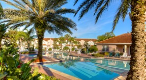 A swimming pool surrounded by palm trees and lounge chairs, with a building in the background. - Fiesta Key 1228 (Kissimmee)