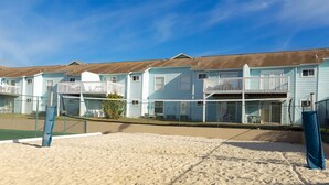 A row of beach houses with balconies, a sandy beach, and a clear blue sky.