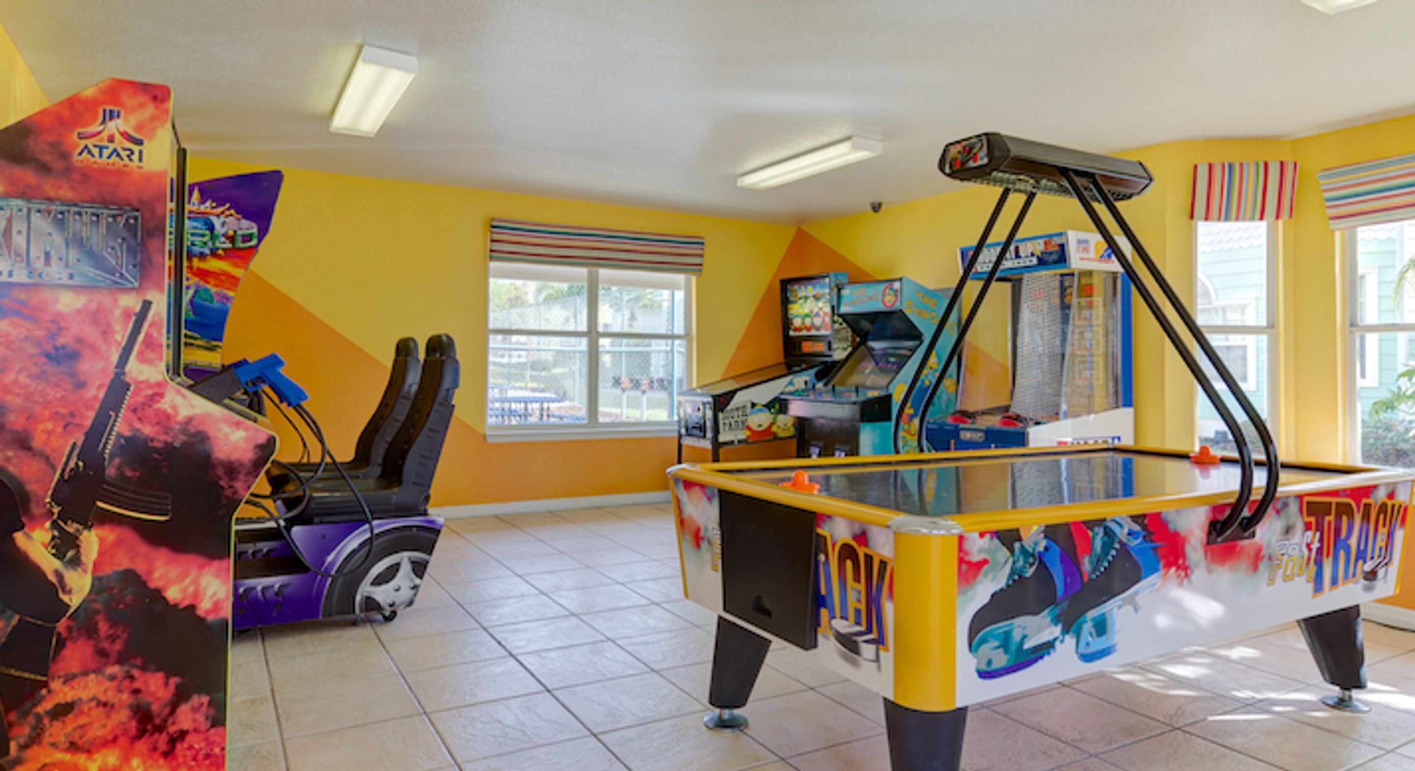 A brightly lit indoor space with arcade games, including a racing game and a claw machine, and a pool table with colorful graffiti.