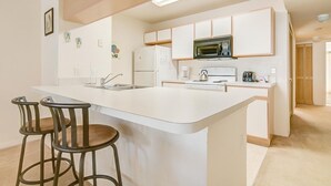 A modern kitchen with a central island, bar stools, a microwave, and a refrigerator.