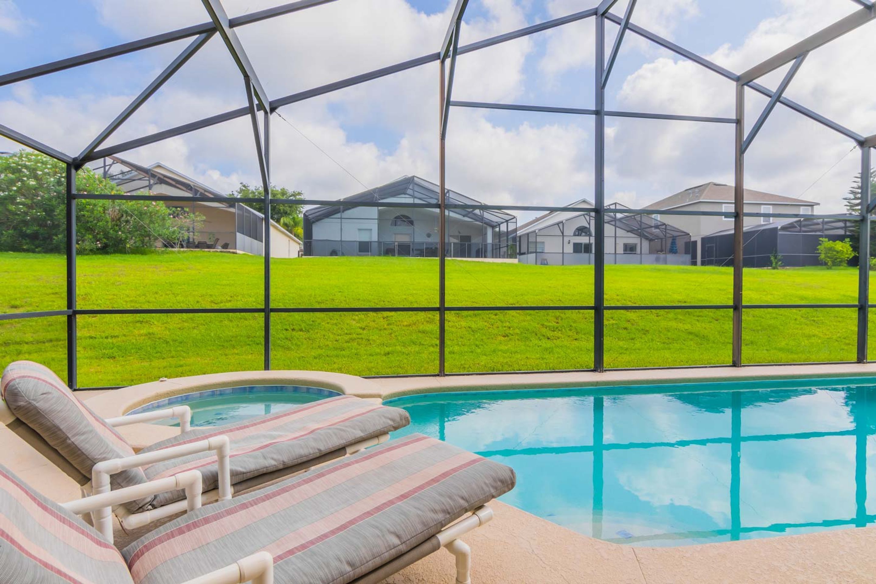 A pool area with a glass enclosure, a lounge chair, and a view of a green lawn and houses in the background.