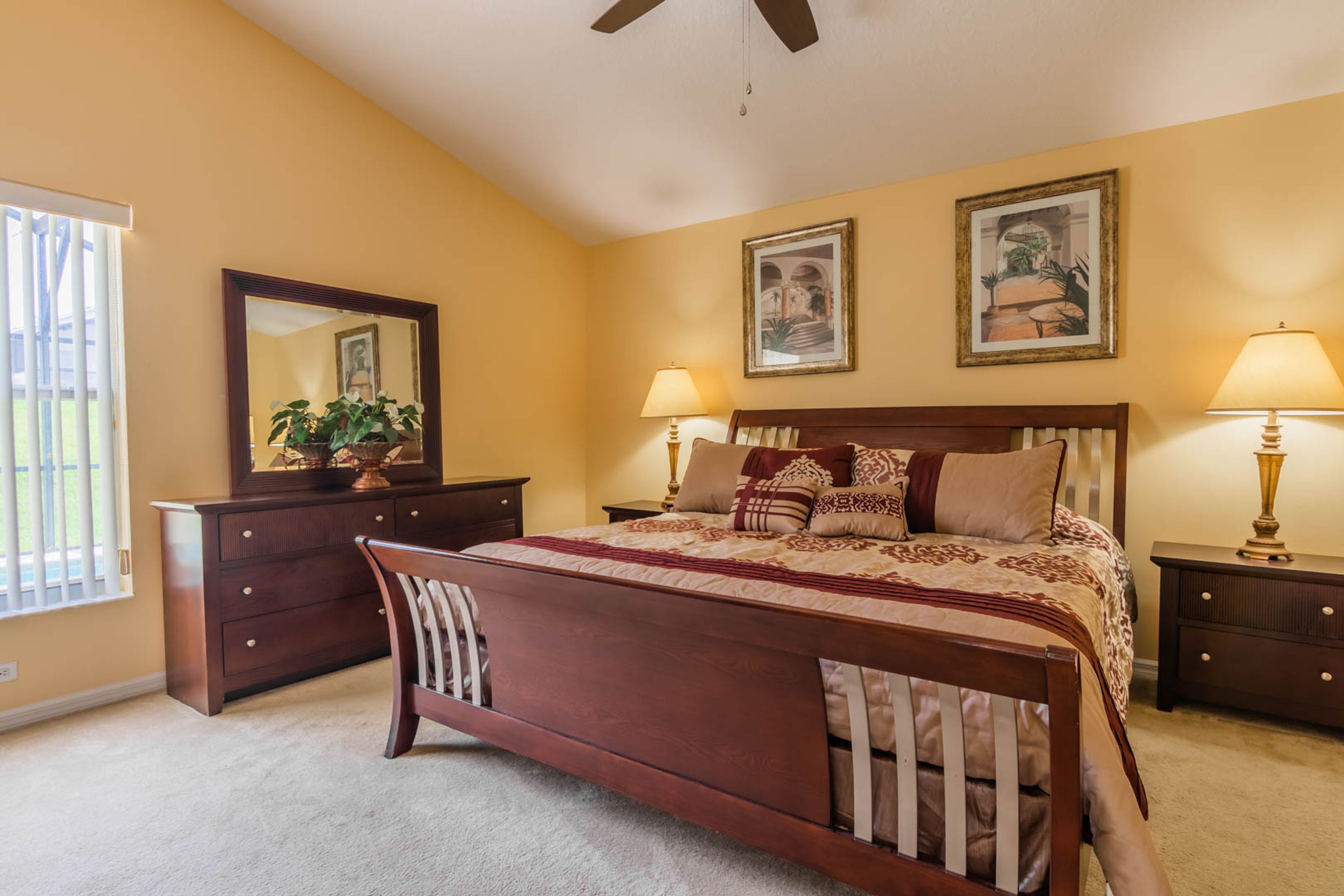 A bedroom with a large bed, a dresser, a nightstand, a lamp, and a ceiling fan.