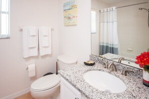 A bathroom with a white toilet, a sink with a granite countertop, a mirror, and a shower curtain.
