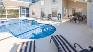 Un área de piscina exterior moderna con sillones reclinables, una mesa de comedor y un porche cubierto.