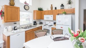 A modern kitchen with wooden cabinets, white appliances, and a dining area with chairs. - Southern Dunes 2401 (Haines City)