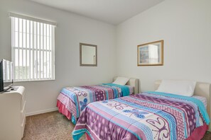 Quarto com duas camas, uma escrivaninha e uma janela com persianas.