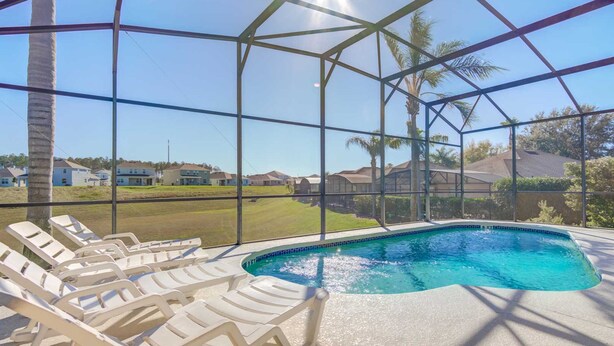 Piscina con lettini, circondata da una struttura in vetro che offre vista su case e palme.