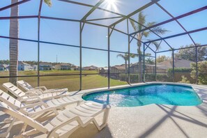 A swimming pool with lounge chairs, surrounded by a glass enclosure with a view of houses and palm trees. - Calabay Parc 467 (Davenport)