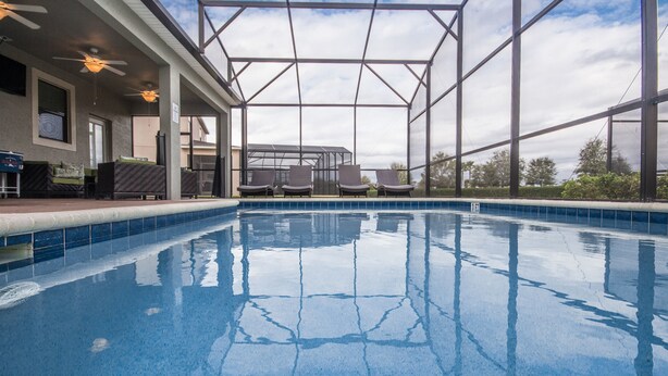 An indoor swimming pool with clear blue water, surrounded by a covered patio area with seating and a view of the sky. - Providence 2401 (Davenport)