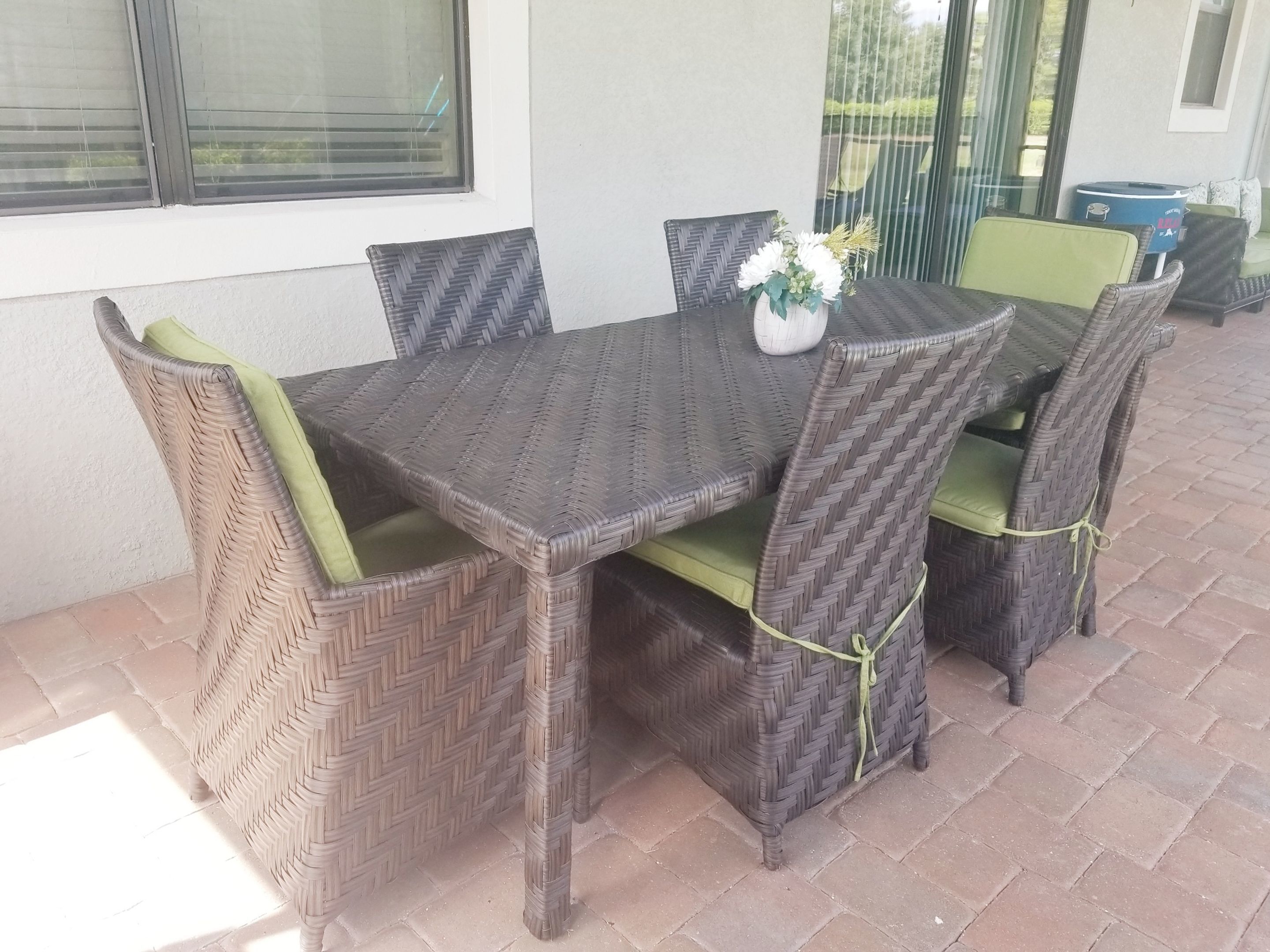 Un juego de comedor de mimbre con cojines verdes, un florero con flores y una ventana al fondo.