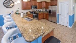 A kitchen with granite countertops, wooden cabinets, stainless steel appliances, and a bar area with white bar stools. - Providence 2401 (Davenport)