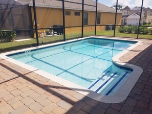 A rectangular swimming pool with a tiled edge, surrounded by a brick patio.