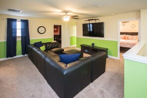 A living room with a black leather sofa, a flat-screen TV, and a green accent wall.