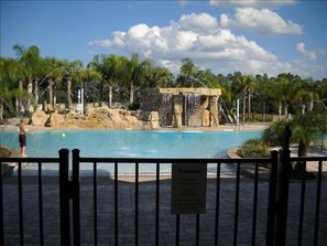 A swimming pool with a waterfall feature, surrounded by palm trees and a stone structure.