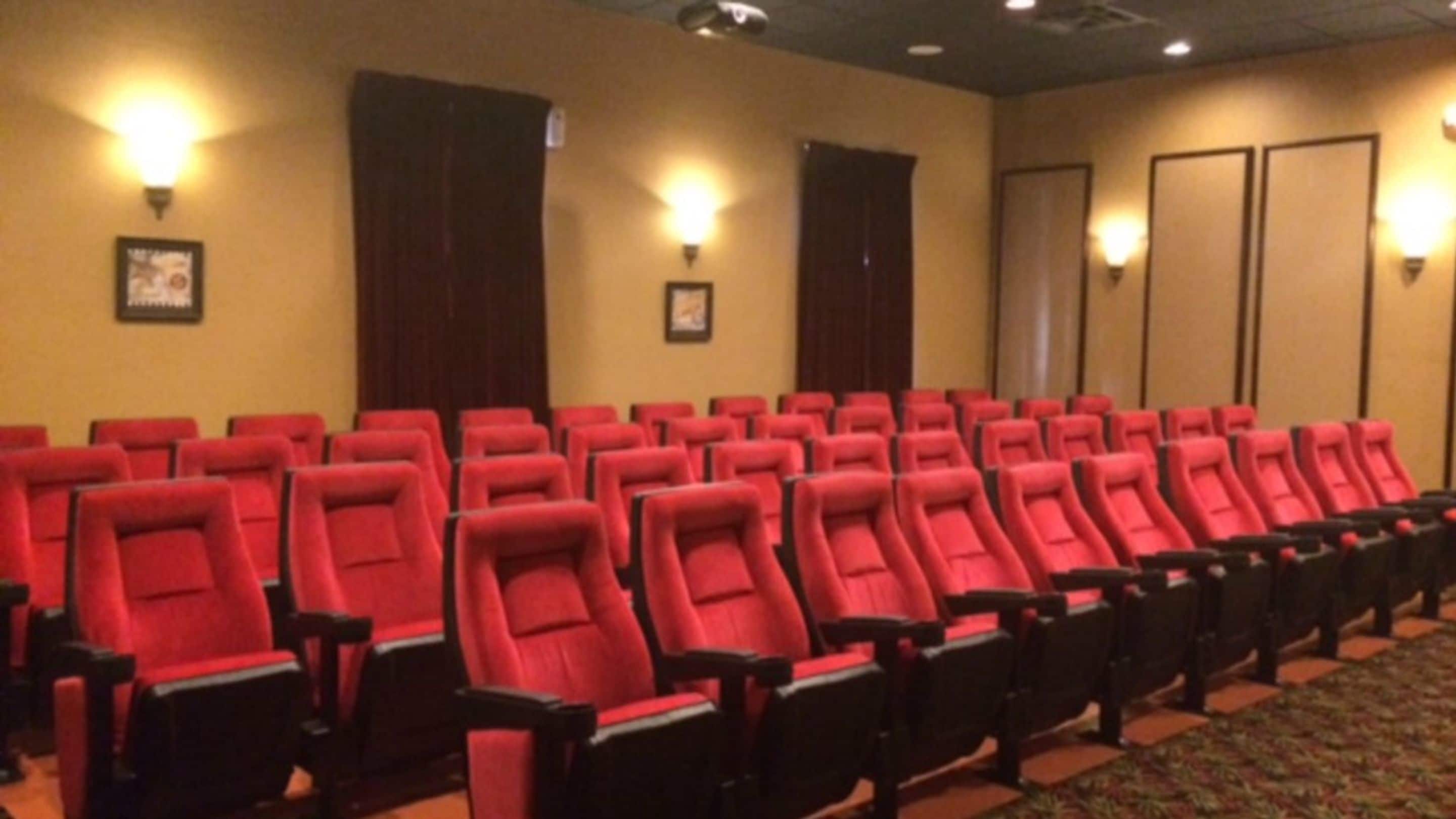 A conference room with rows of red chairs, wooden tables, and wall-mounted lights.