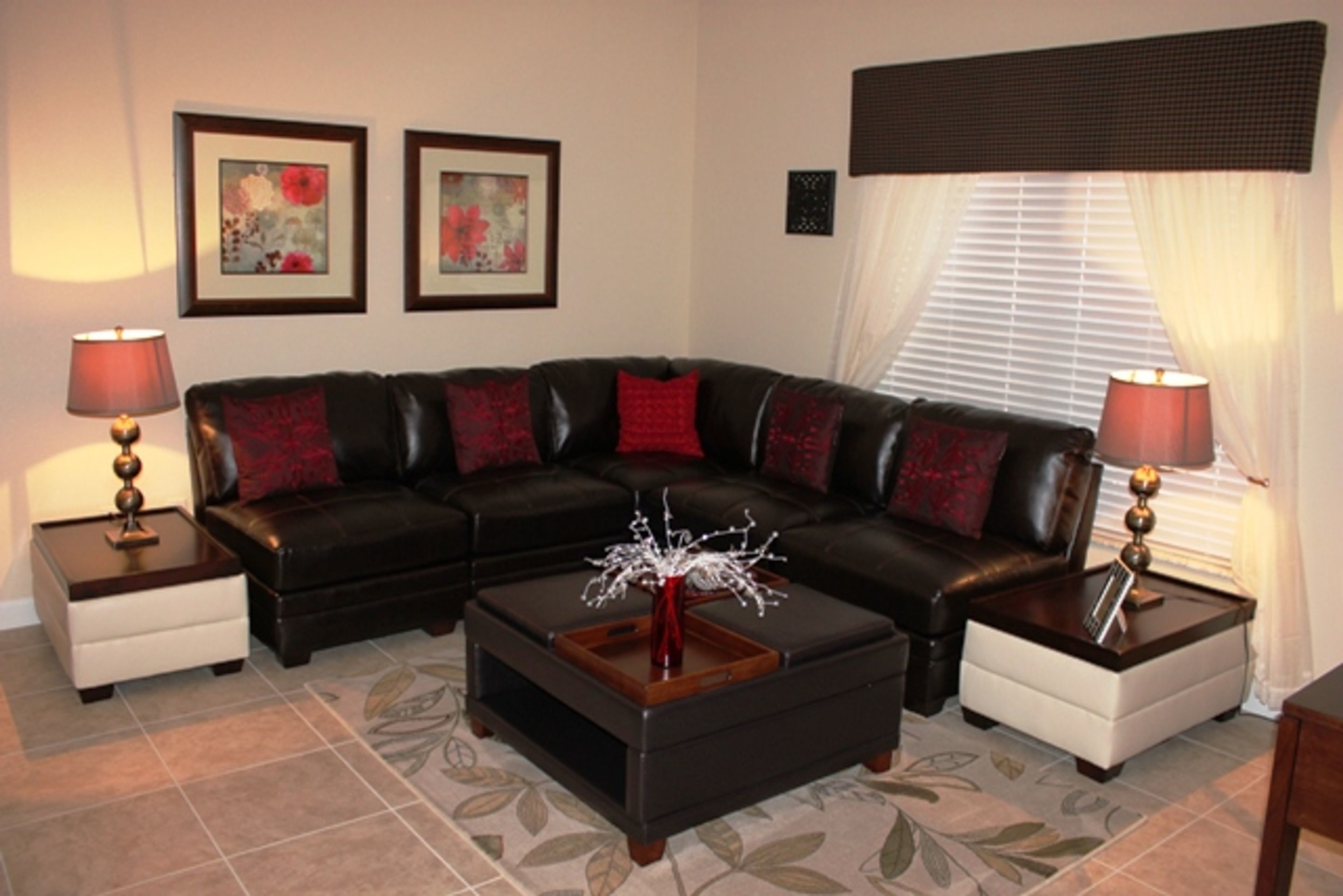 A living room with a black leather sectional sofa, two side tables with lamps, a decorative vase on a wooden coffee table, and a patterned rug.