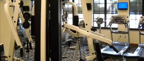 A gym with various exercise equipment, a treadmill, and a television screen.