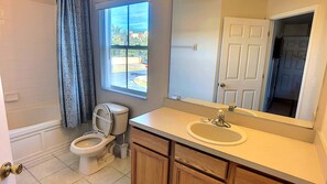 A bathroom with a toilet, sink, mirror, and window. - Regal Oaks 2716 (Kissimmee)