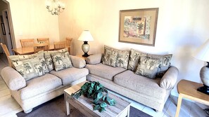 A living room with a sectional sofa, a wooden coffee table, a lamp, and a framed artwork on the wall. - Regal Oaks 2716 (Kissimmee)