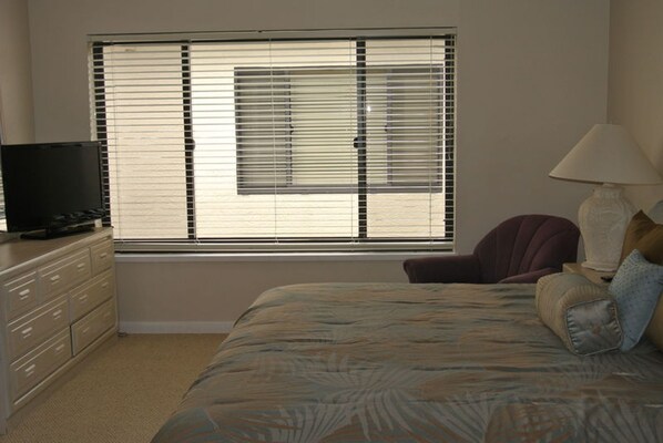 A bedroom with a bed, a dresser, a chair, a lamp, and a window with blinds.