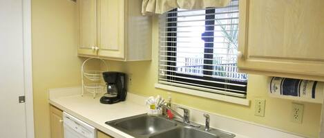 A compact kitchen with two sinks, a coffee maker, and a window with blinds.