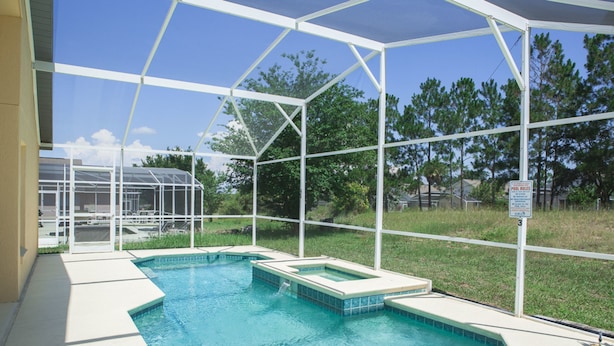A swimming pool with a glass enclosure, surrounded by a grassy area and trees. - Westridge 1007 (Davenport)