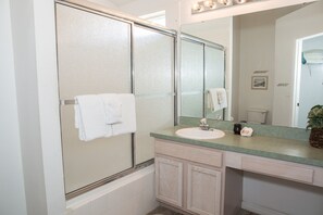 A bathroom with a glass shower enclosure, a sink with a mirror above it, and a towel hanging on the wall. - Westridge 1007 (Davenport)