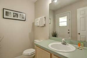 A bathroom with a toilet, sink, mirror, and framed pictures on the wall.
