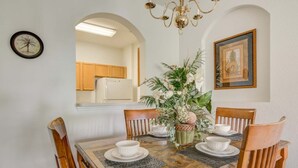 A dining area with a wooden table set for four, surrounded by chairs. A chandelier hangs above, and there are framed pictures on the walls. - Windsor Hills 7675 - 303 (Kissimmee)