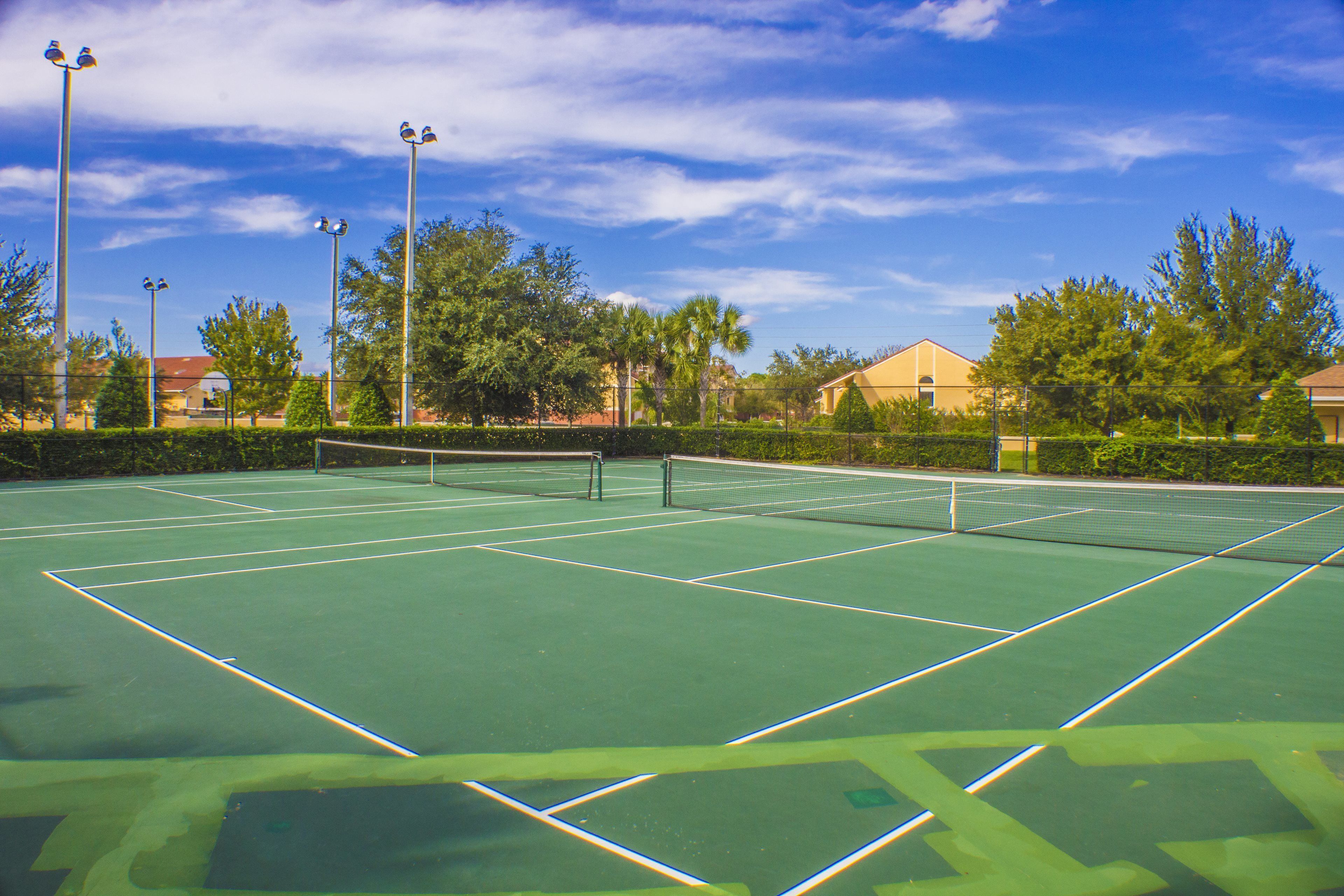 An outdoor tennis court with a net, surrounded by trees and buildings.