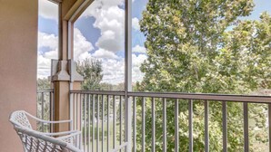 A balcony with a white chair, a metal railing, and a view of trees and a partly cloudy sky. - Windsor Hills 7675 - 303 (Kissimmee)