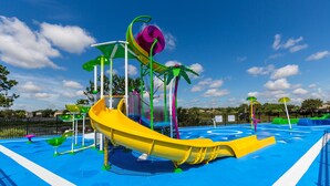 A water park with a yellow slide, green and purple play structures, and a blue pool area. - Windsor Hills 7675 - 303 (Kissimmee)