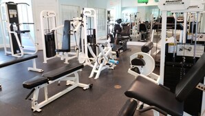Une salle de sport équipée de divers appareils d’exercice, de bancs et d’un écran de télévision fixé au mur.