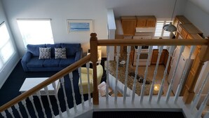 Un vaste espace de vie avec un canapé bleu, un escalier en bois et une cuisine à l’arrière-plan.