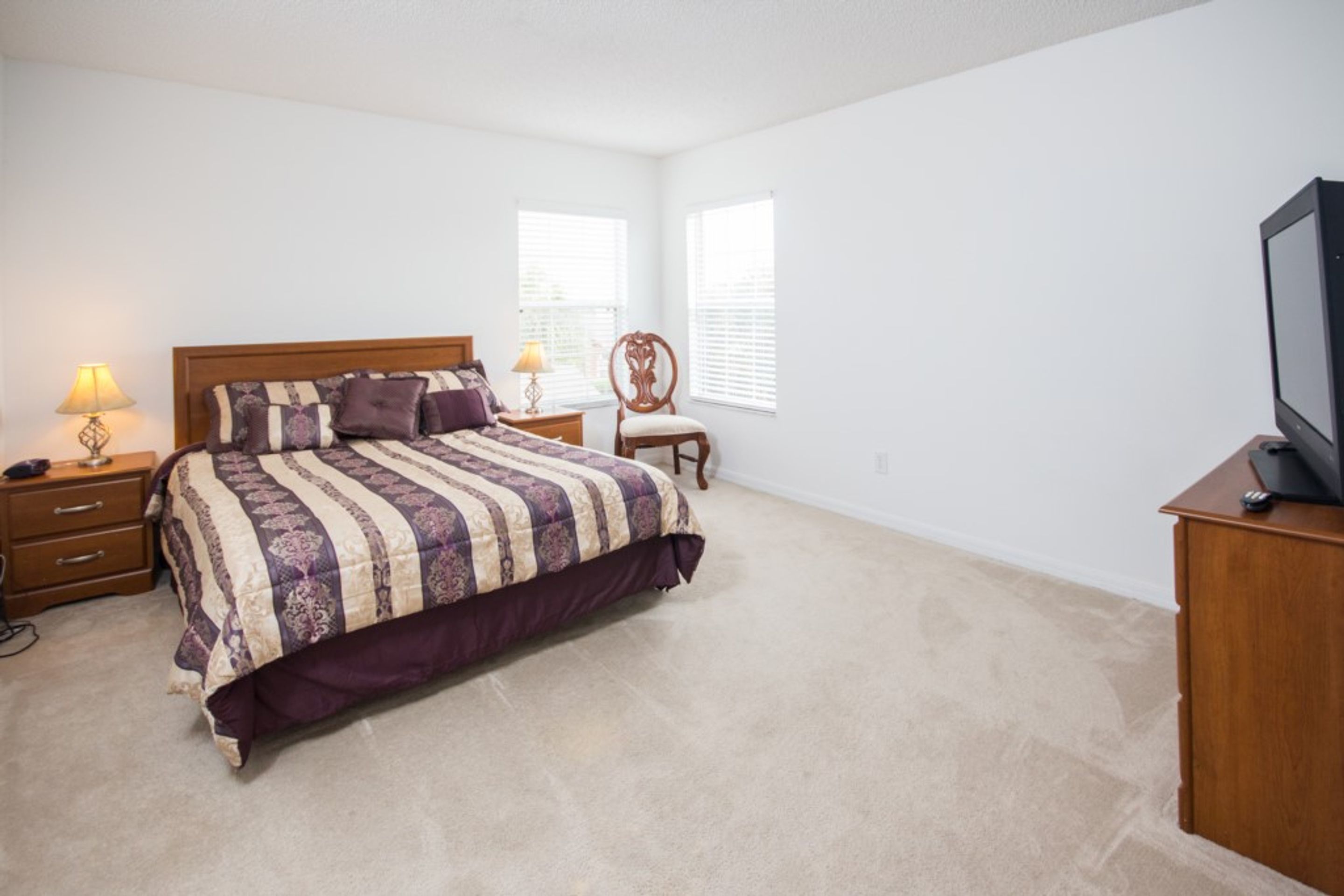 A bedroom with a large bed, two bedside tables, a chair, and a TV stand.