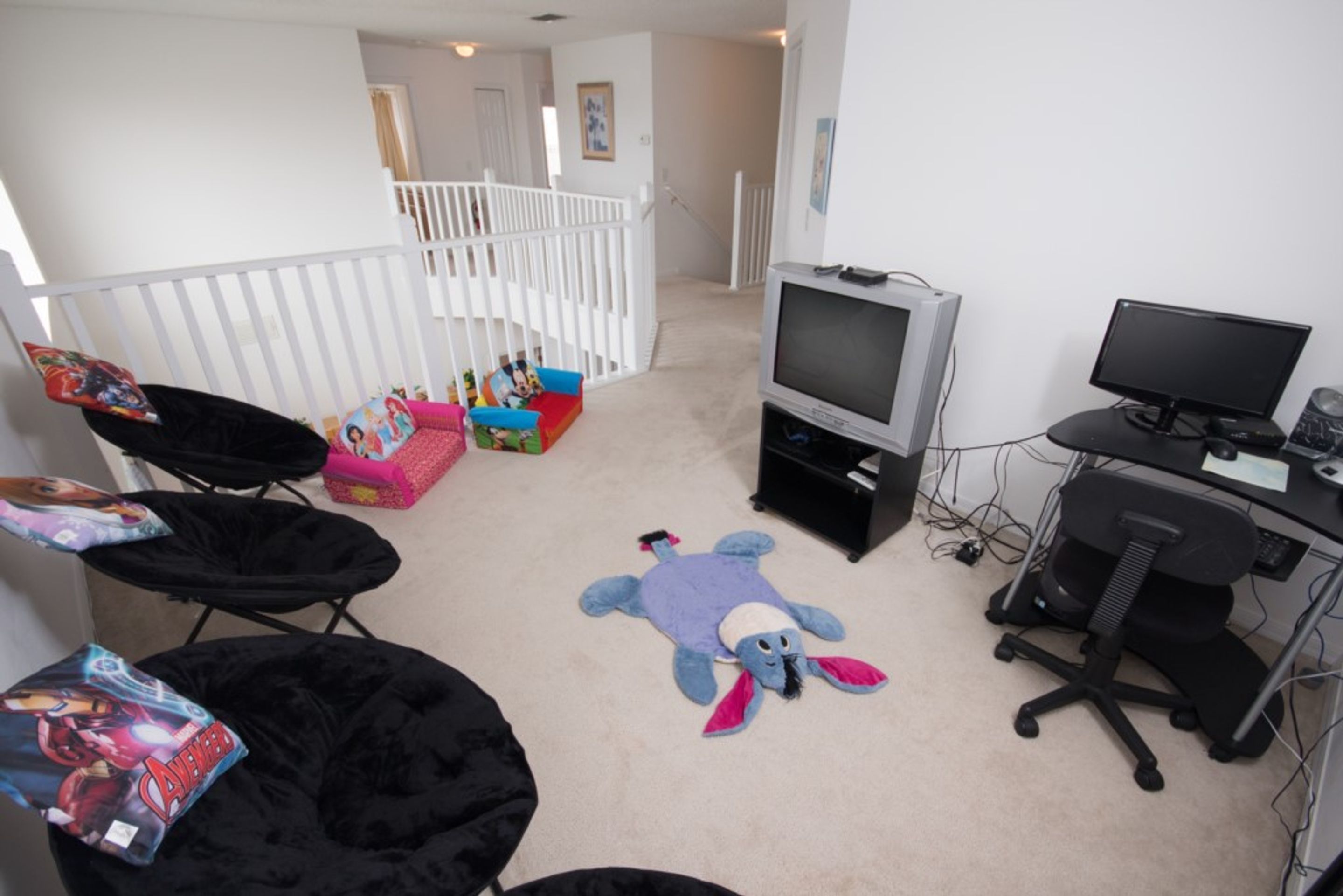 Ein Wohnzimmer mit Fernseher, Bürostuhl und weichen Spielzeugen auf dem Boden.