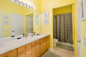 A bathroom with a yellow wall, a white sink, wooden cabinets, a mirror, and a shower curtain.