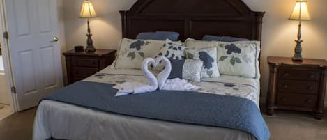 A neatly made bed with a blue and white bedspread, two bedside lamps, and floral pillows.