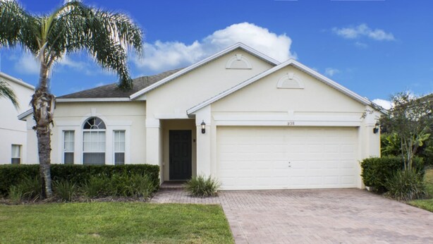 A single-story house with a garage, a front door, and a small front yard with a palm tree and shrubs. - High Gate Park 938 (Davenport)