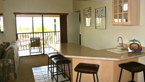 A kitchen with a large island, bar stools, a sink, and a window overlooking a patio.