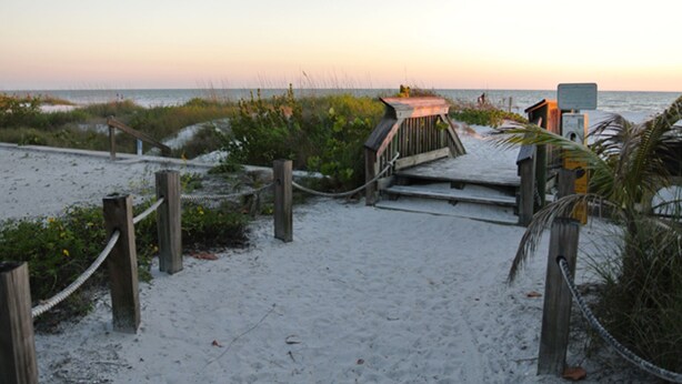 A wooden boardwalk leading to a beach area with a wooden structure and a sign.