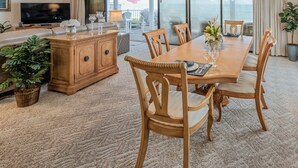 Un salon spacieux avec une grande table à manger en bois, des sièges confortables, un téléviseur à écran plat et une vue sur l’extérieur grâce à de grandes portes coulissantes.