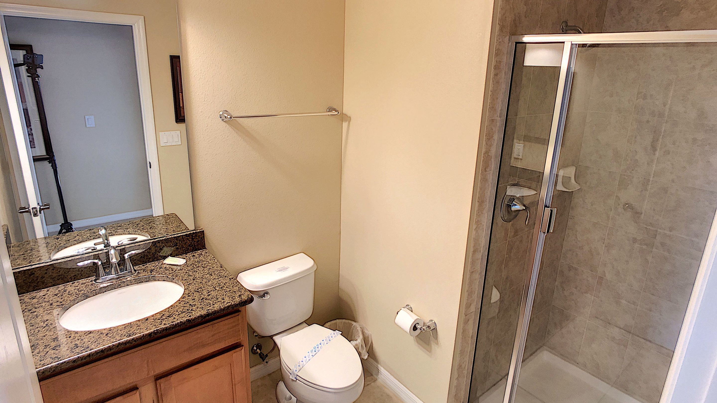 A bathroom with a granite countertop sink, a toilet, and a glass-enclosed shower.