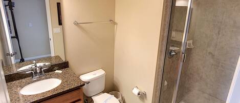 A bathroom with a granite countertop sink, a toilet, and a glass-enclosed shower.