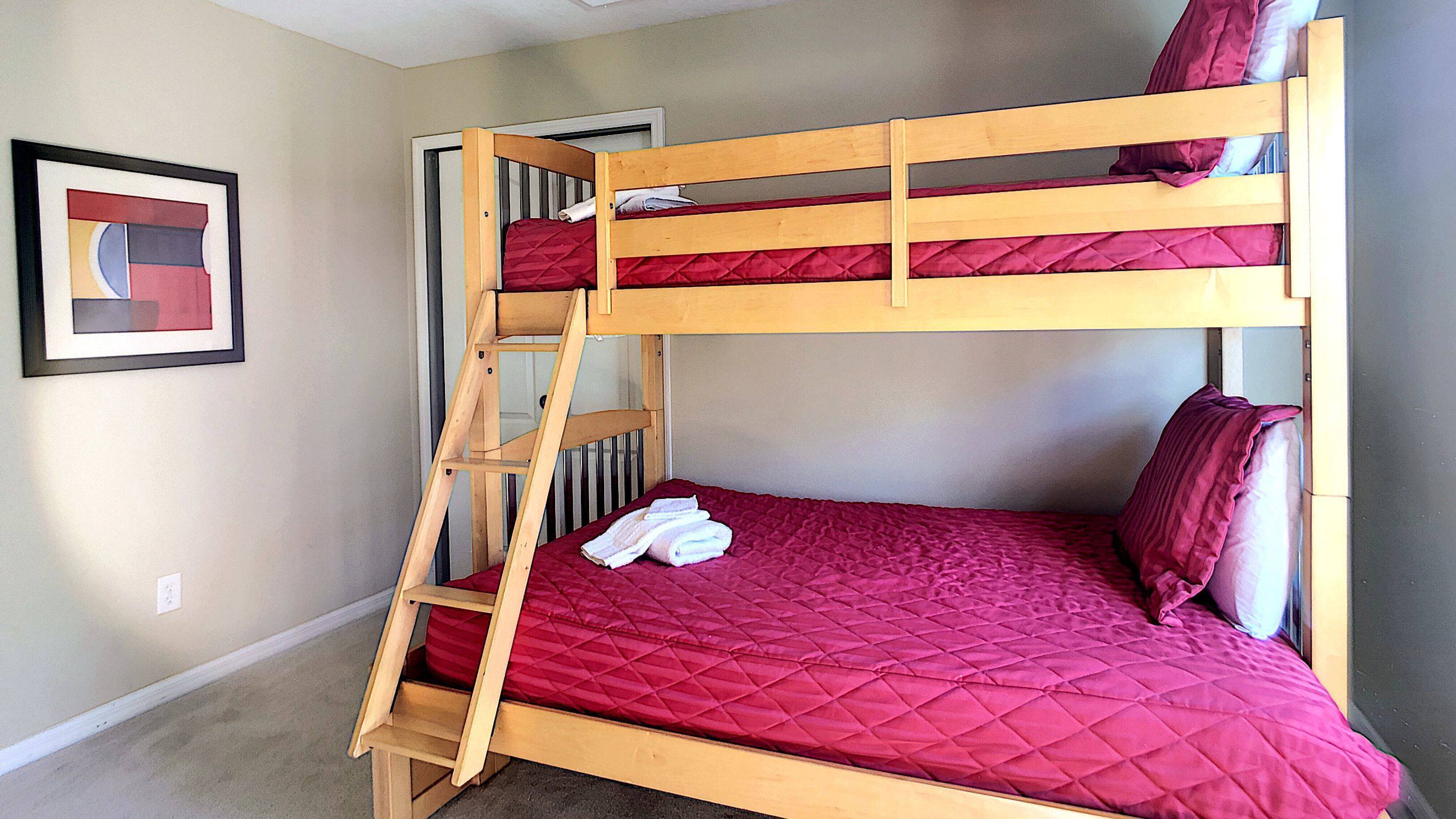 Ein Etagenbett mit einer rot gesteppten Matratze, einer Holzleiter und einem weißen Handtuch auf der unteren Etage.