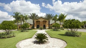 A large, two-story building with a symmetrical facade, central entrance, and a landscaped garden with palm trees and a central palm plant. - Paradise Palms 8965 Candy (Kissimmee)