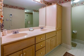 A bathroom with two sinks, wooden cabinets, a large mirror, and a hairdryer on the wall. - Fort Myers Beach Area 7327 - 202 (Fort Myers Beach)