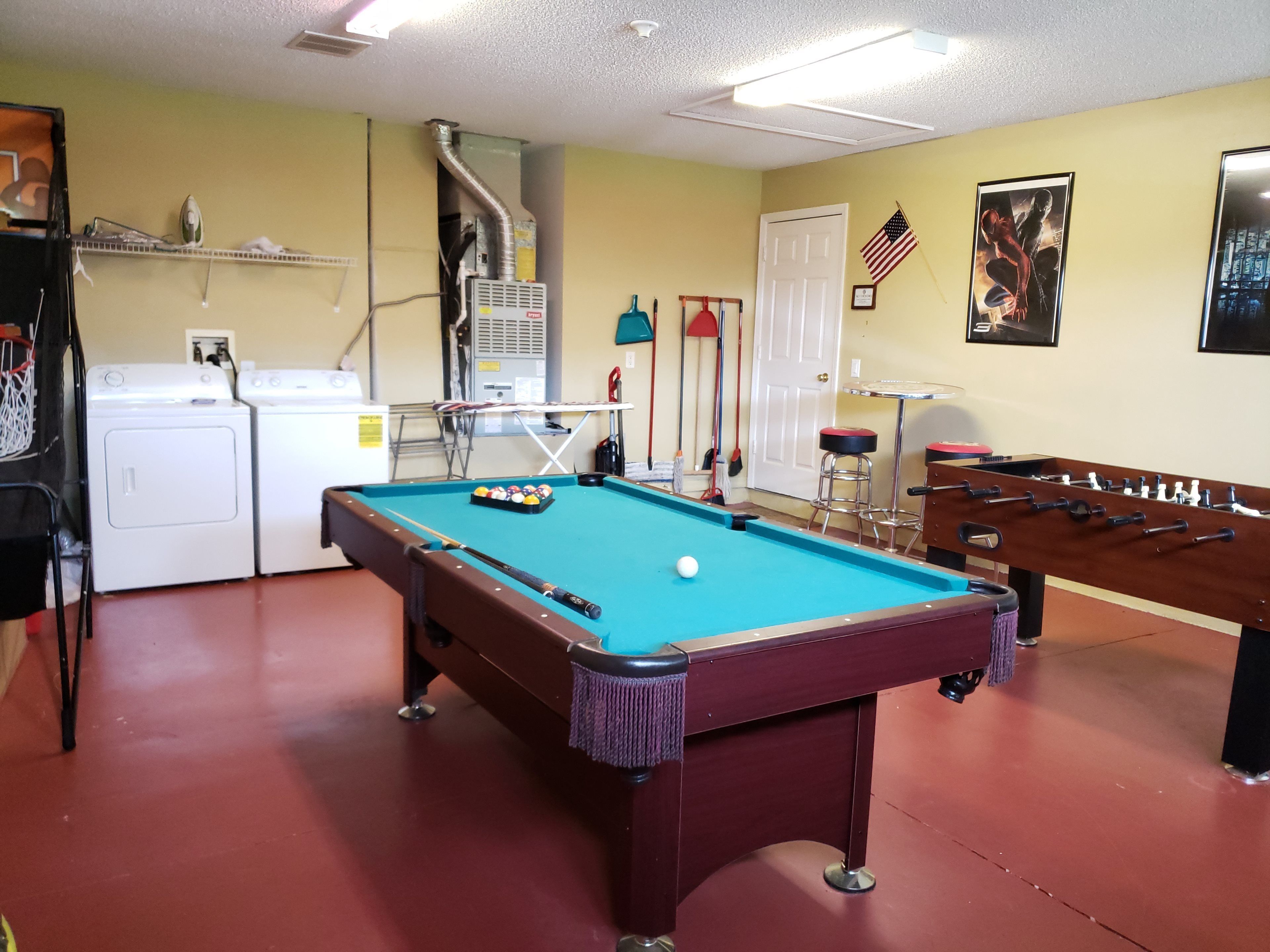 Une table de billard, une table de baby-foot, un lave-linge et un sèche-linge se trouvent dans une pièce aux murs jaunes.
